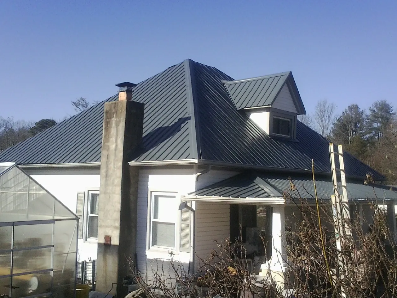 Dark blue standing seam metal roof on a white farmhouse with dormer — Slate & Tile Roof Repair by Roofing Brothers in Ferrum
