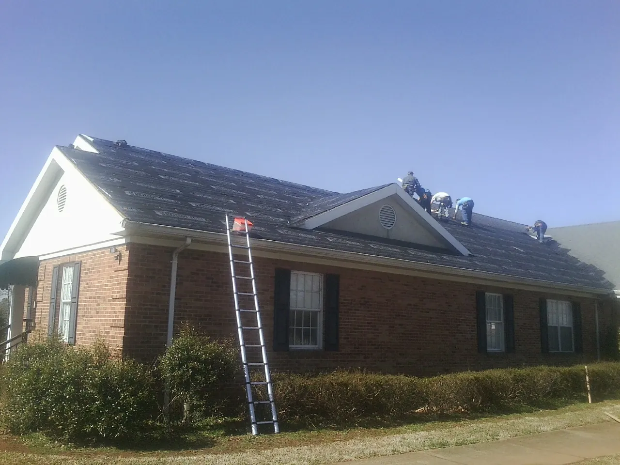 Crew tearing shingles off a brick ranch roof with a ladder set — Emergency Roof Repair work by our crew in Ferrum