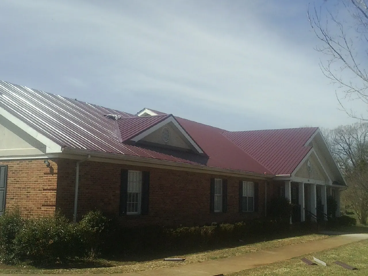 Red metal roof with gabled entries on a long brick building, from a Hail Damage Roof Repair job in Ferrum