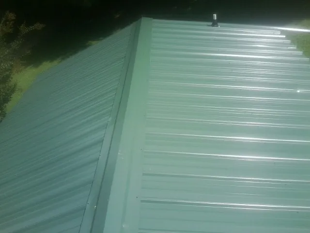 New green metal panels meeting at the ridge of a roof — Flat Roof Repair work by our crew in Ferrum